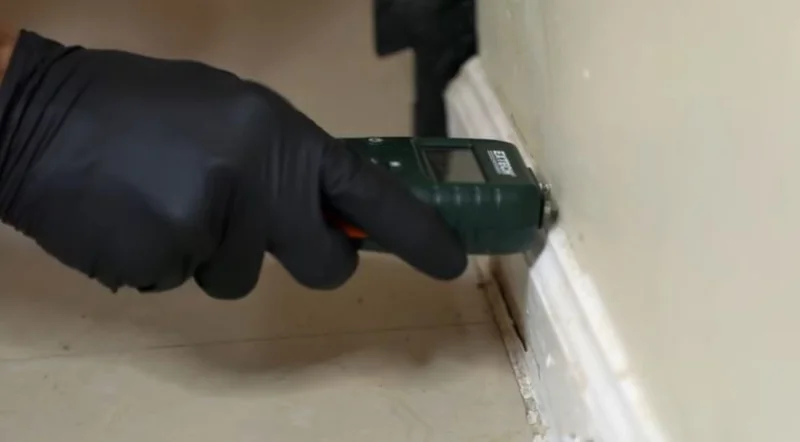 Technician checking a baseboard for hidden moisture with a pin moisture meter