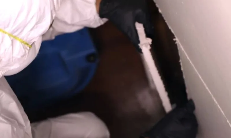 Technician in protective gear removing water-damaged drywall